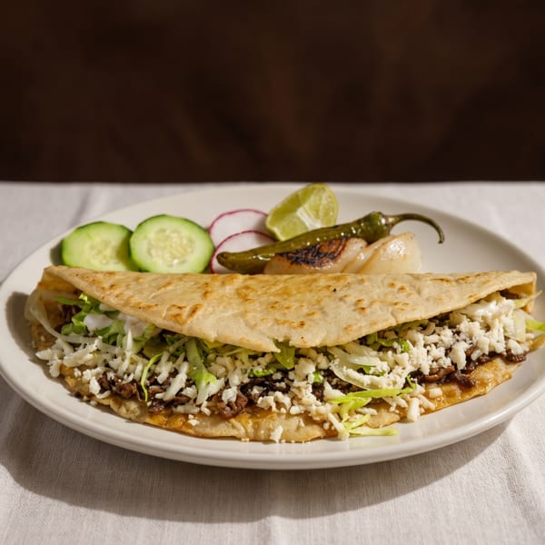 A large quesadilla filled with meat, lettuce, and cheese, served with cucumber, radish, and lime.