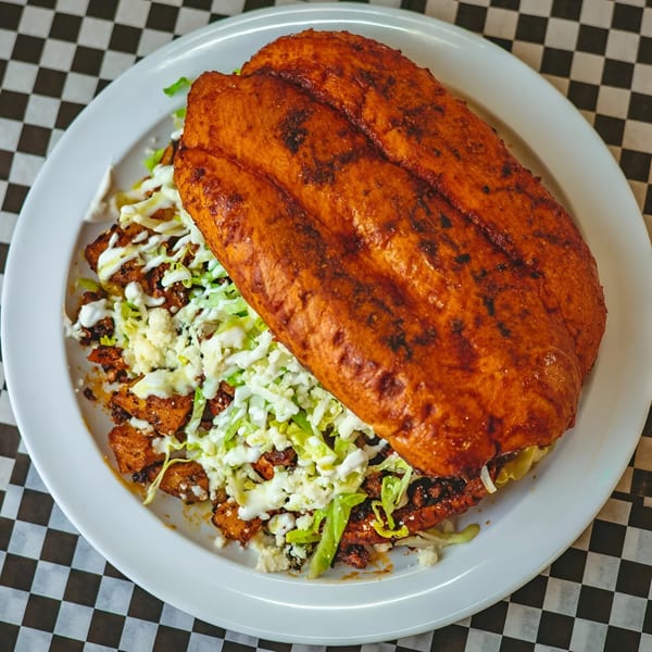 A large, golden-brown Mexican torta with lettuce, cheese, and crema on a white plate.